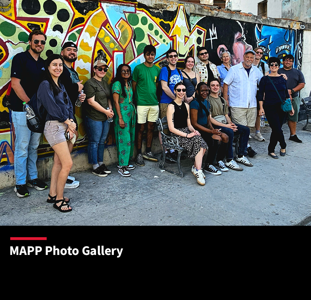 Students and faculty posing in front of a colorful mural