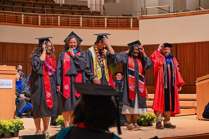 Students in cap and gowns on stage moving their tassles
