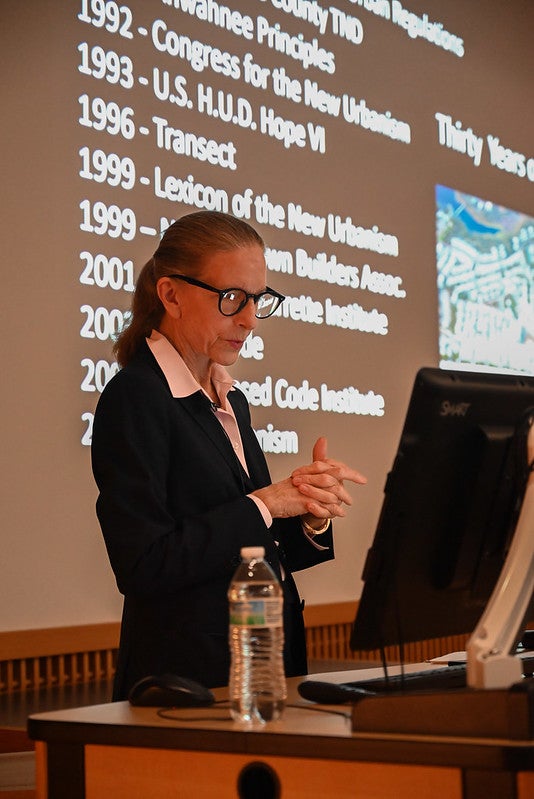 Elizabeth Plater-Zyberk presenting. A screen listing dates is behind her