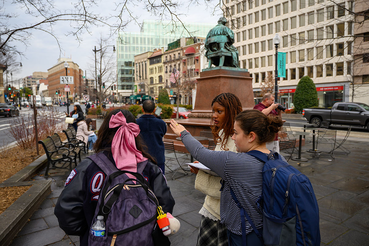 Students on the Longfellow statue plaza pointing out towards the Washington D.C. streets, analyzing their site.