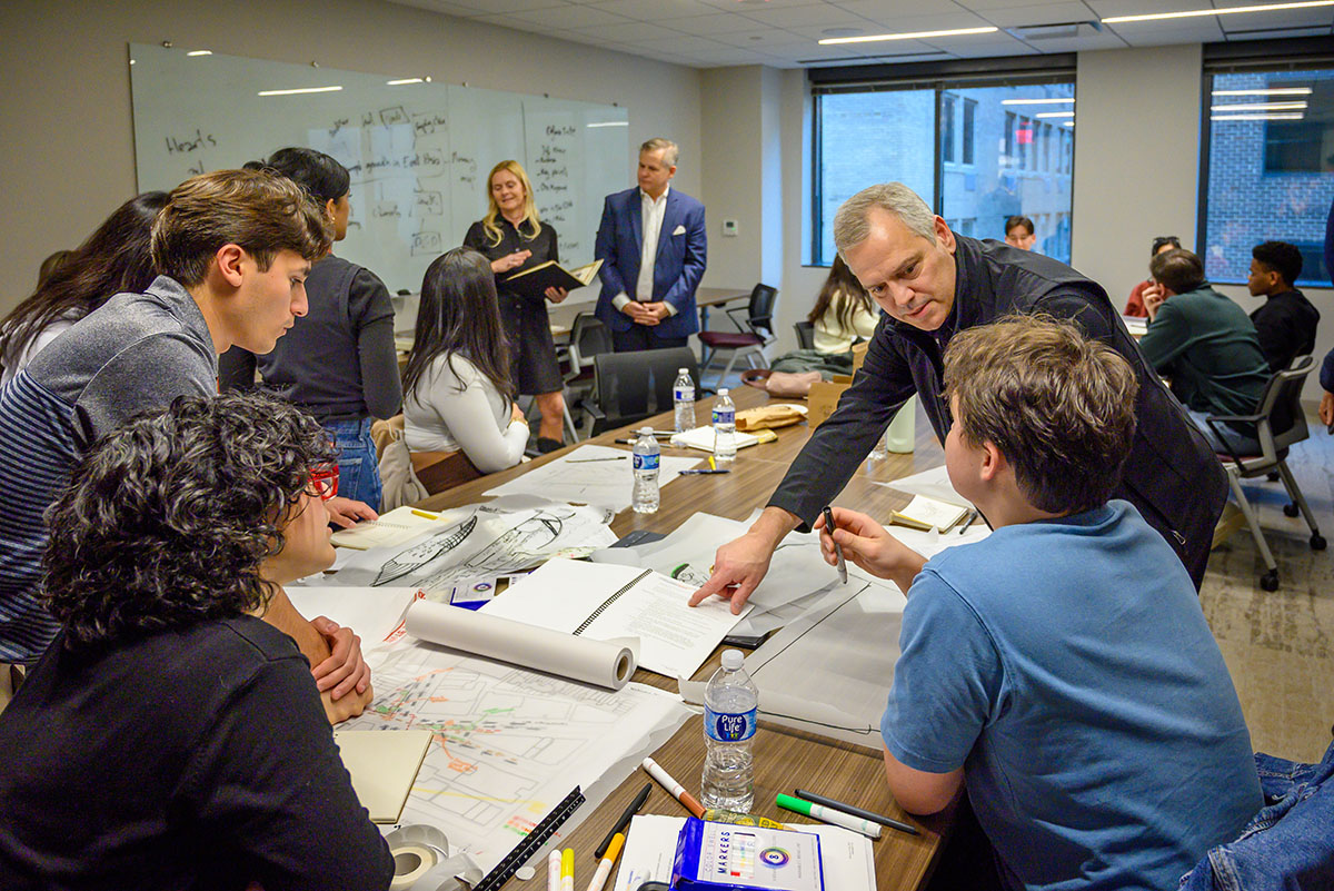 Greg Luhan giving feedback to a student group's site design. Abigail Adams Brigstocke is in the background holding a book and talking to other students.