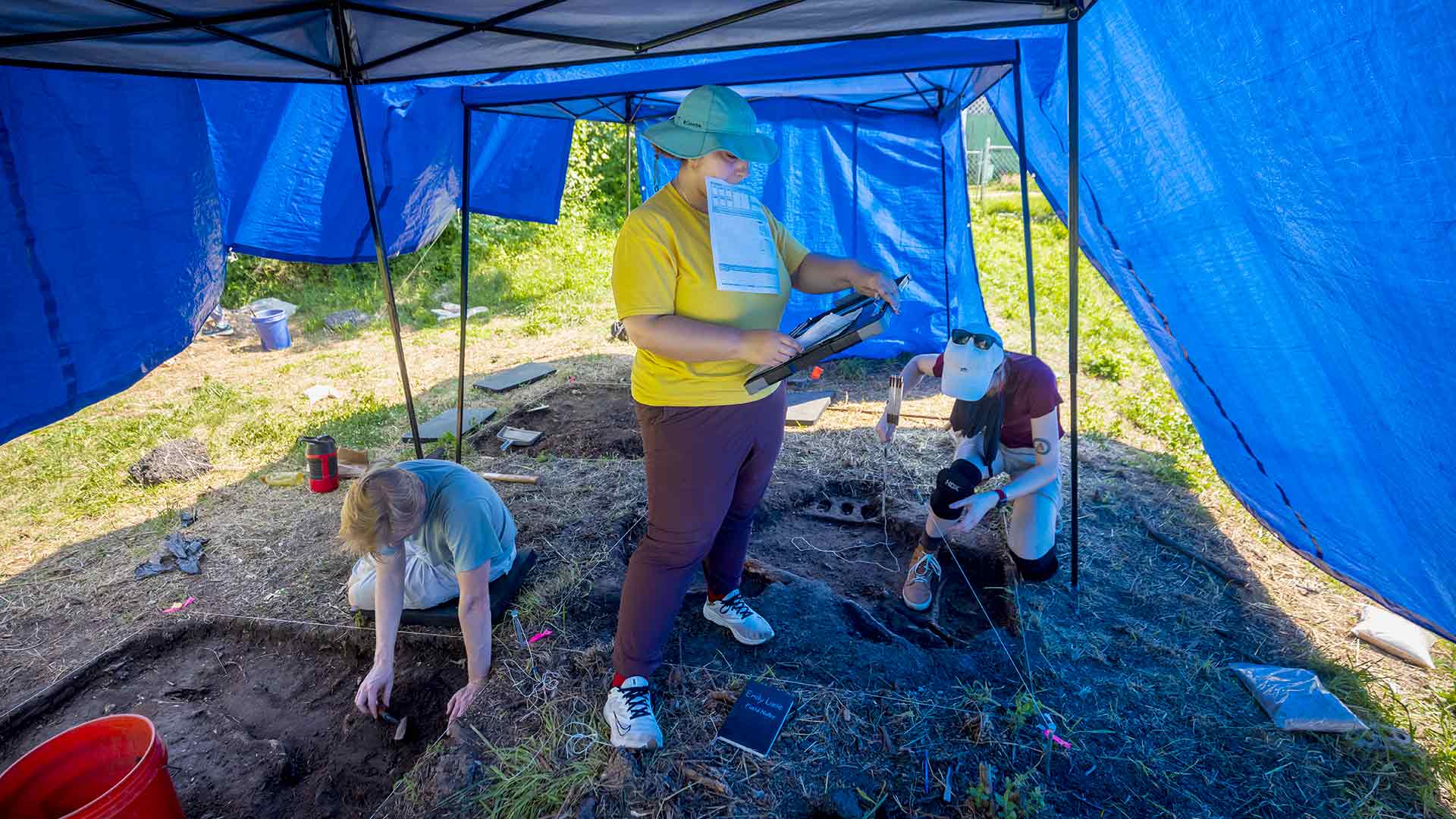 Student in center holding elevation notes and others in the background are excavating 