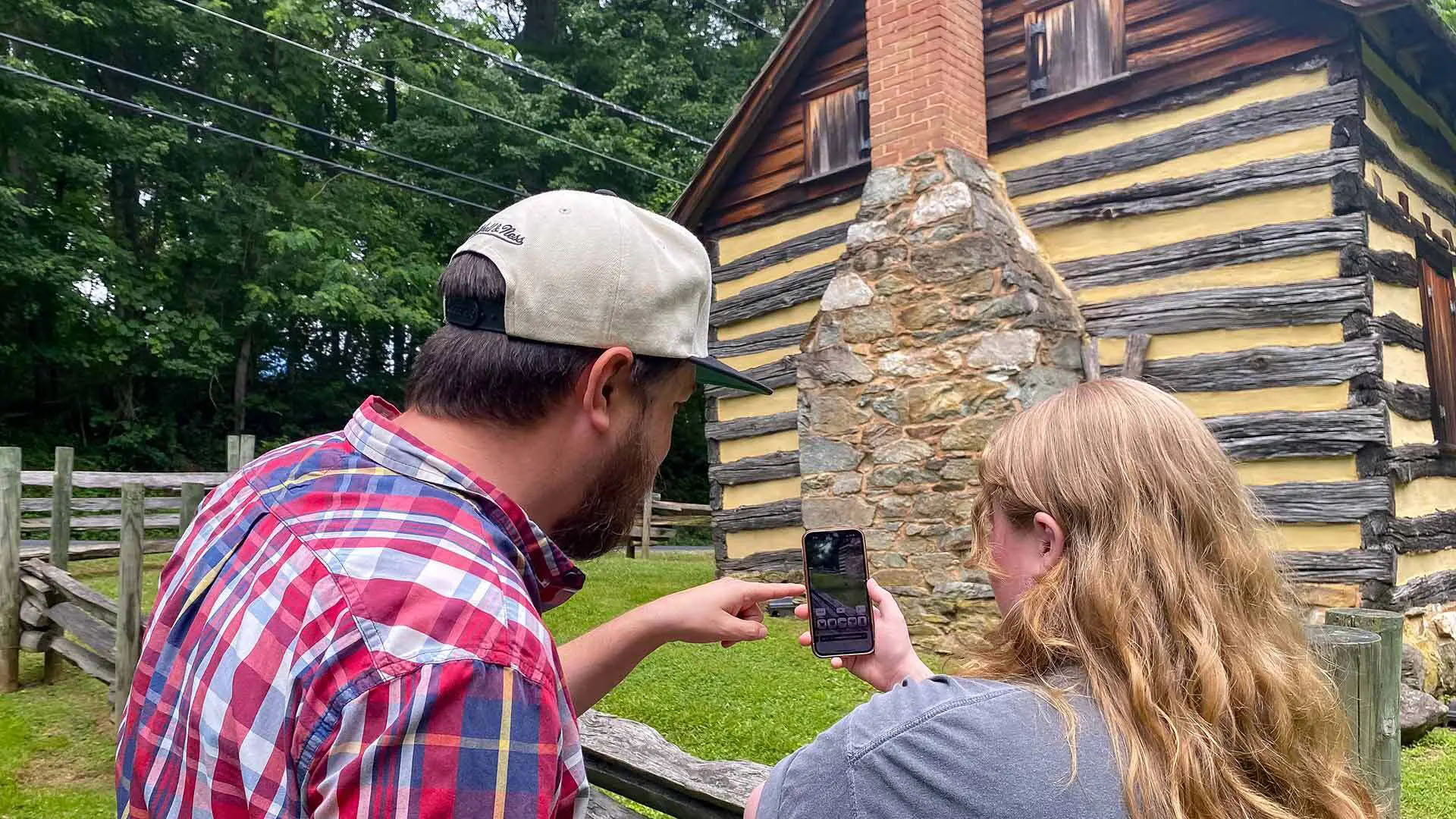 Two people looking at a phone with a wooden cabin in the background