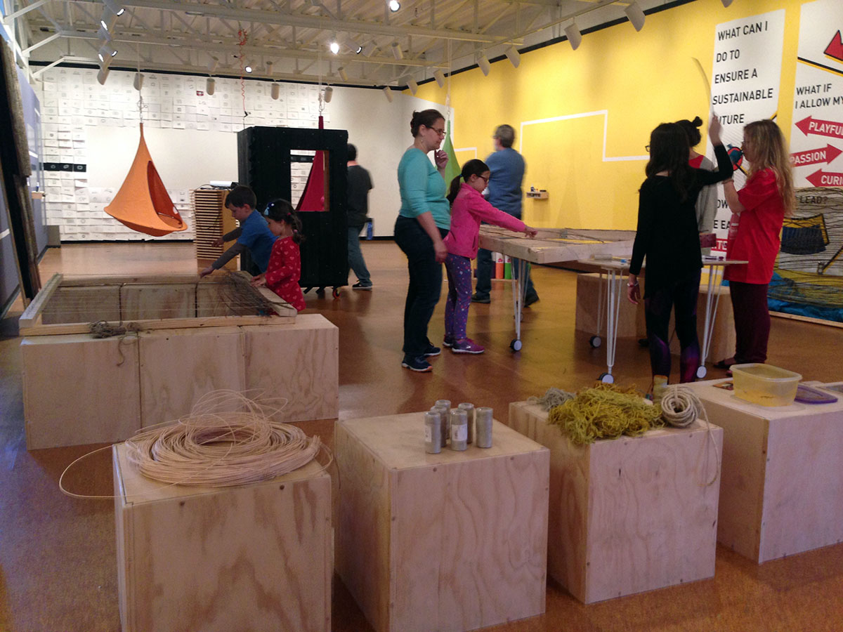 Children playing around wooden structures and touching fabric at the gallery exhibit.