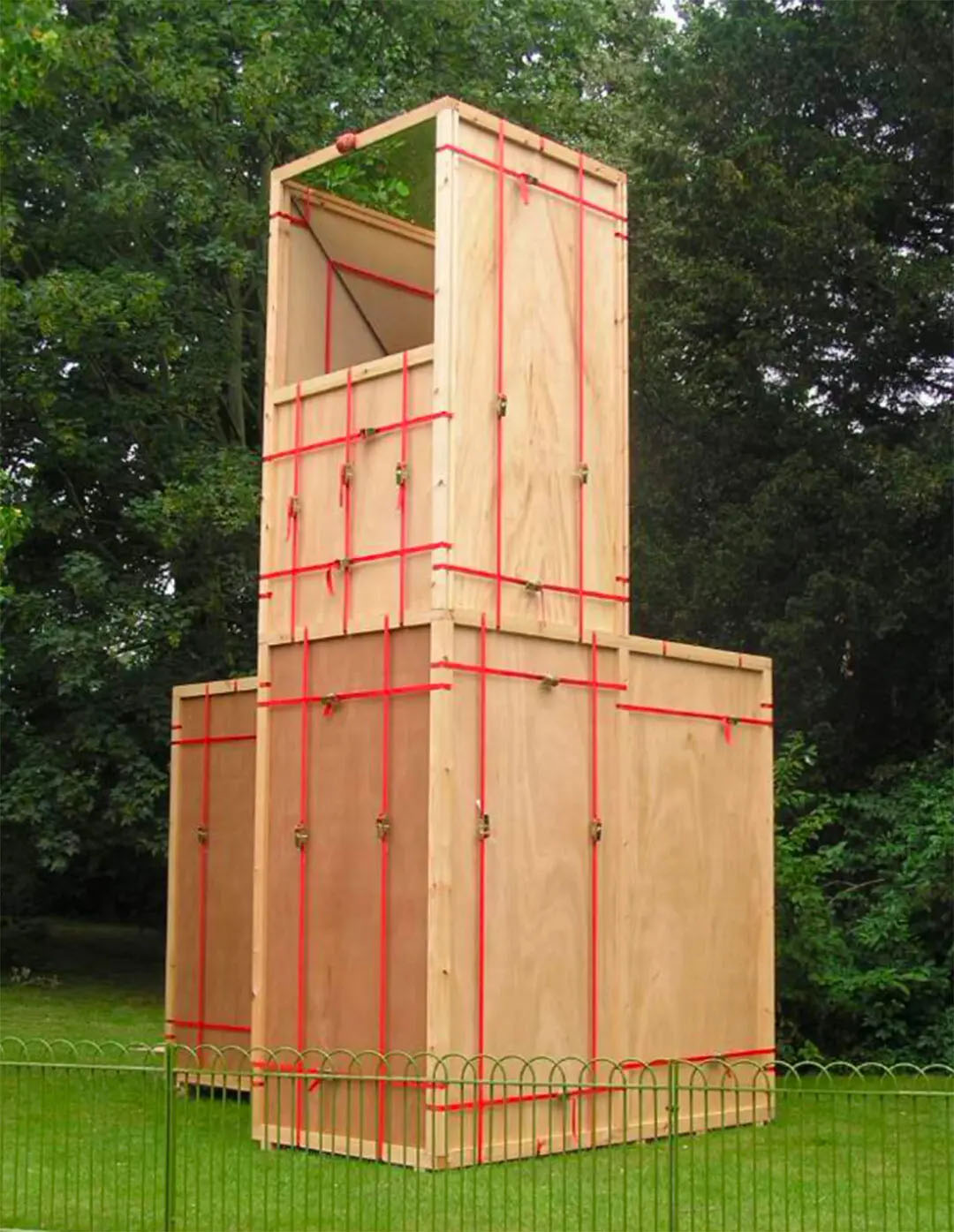 Large wooden boxes with red straps in a green yard.