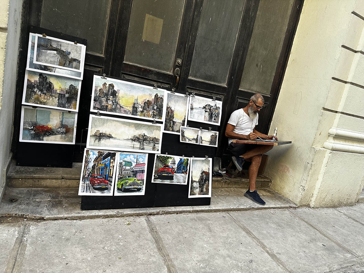 A man painting by his street booth of paintings