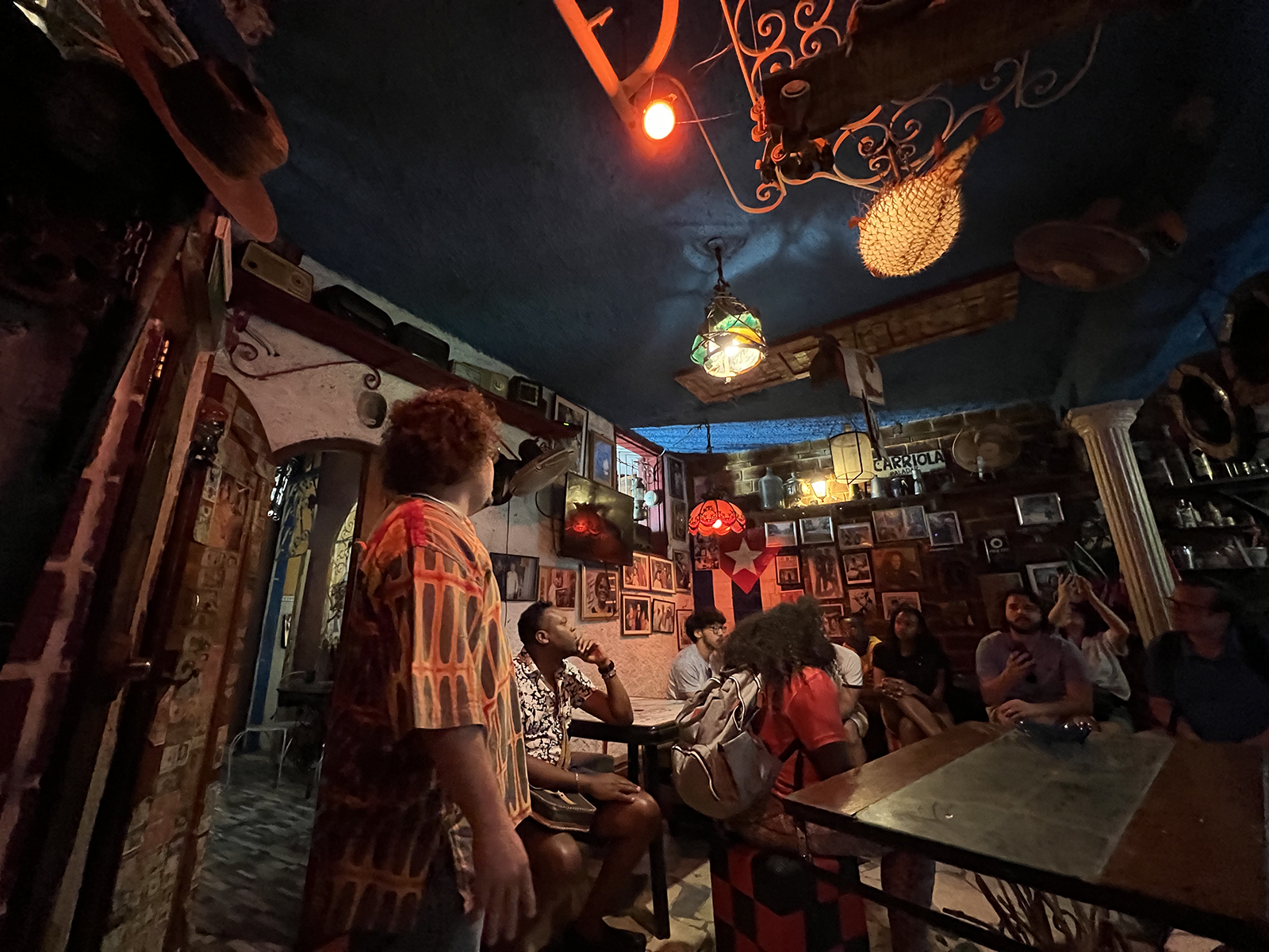 Interior of a Cuban bar filled in warm light and pictures hanging on the walls.