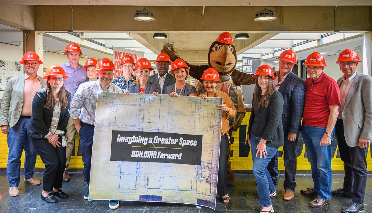 Board of Visitors and Testudo wearing hard hats standing in the mezzanine with a large blueprint that states "Imagining a Greater Space"