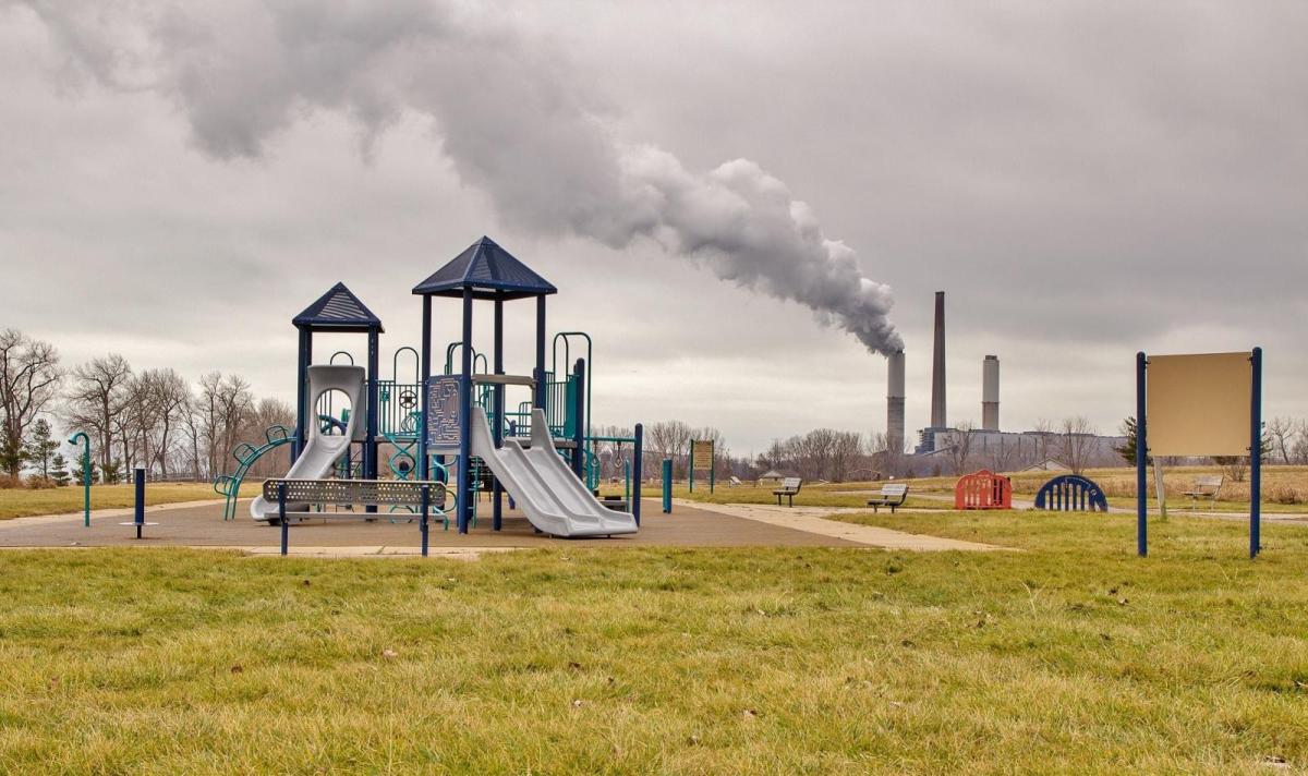 Children's playground with a grey sky in the background and smoke coming out of an industrial site