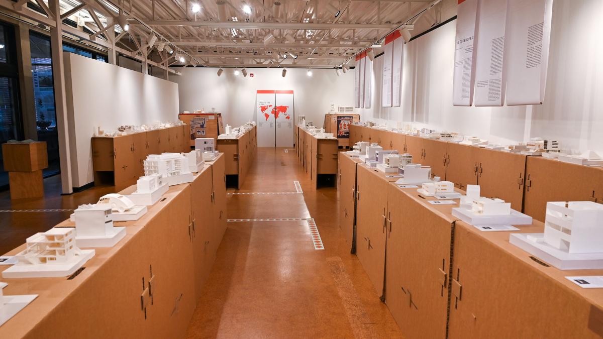 Numerous white architecture building models leading to a large poster in the back with the map of the world in orange
