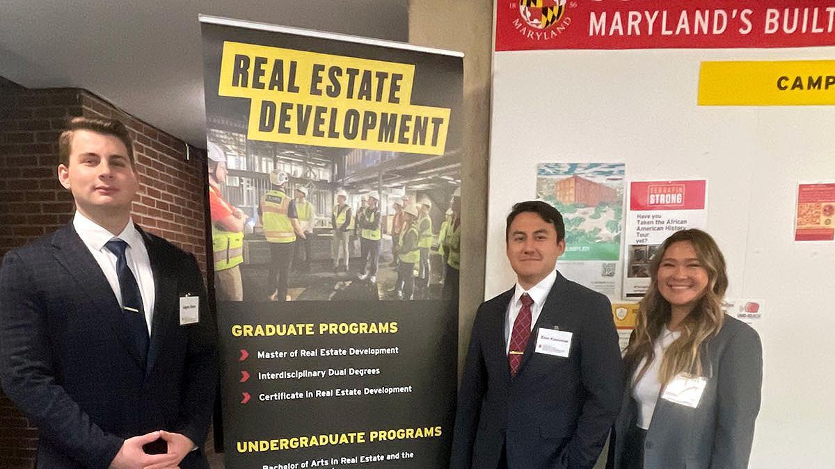 Students in suits standing by a Real Estate Development sign