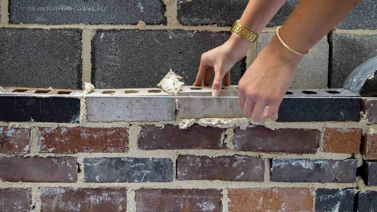 A hand placing a brick on a brick wall. 