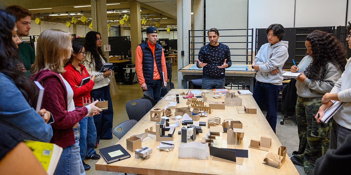 Students looking at models around a table, Professor Abrams is teaching in the middle
