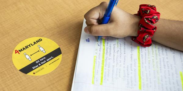 Student writing by a 4Maryland social distance sticker
