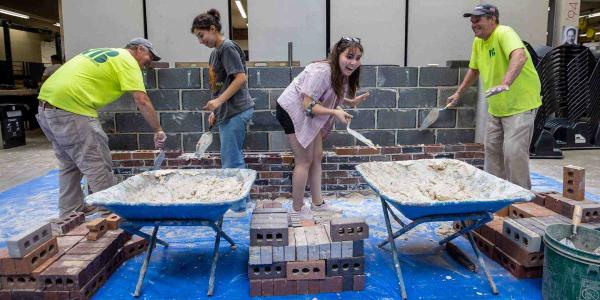 Student laughing while brick laying. Other students and Potomac Valley Brick and Supply workers. 