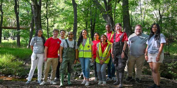 SIRJ Lab team members on a site visit, green trees and a bridge in the background