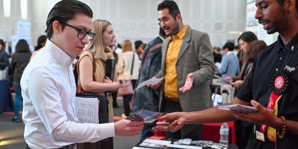 People exchanging pamphlets and others talking in the background during a career fair.