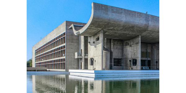 A concrete building with undulating roof, and its reflection in a pond