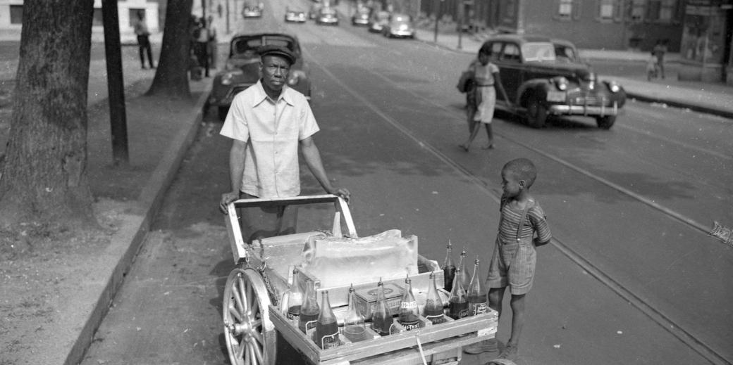 Young boy by a snowball vendor in 1940s Harlem Park. 