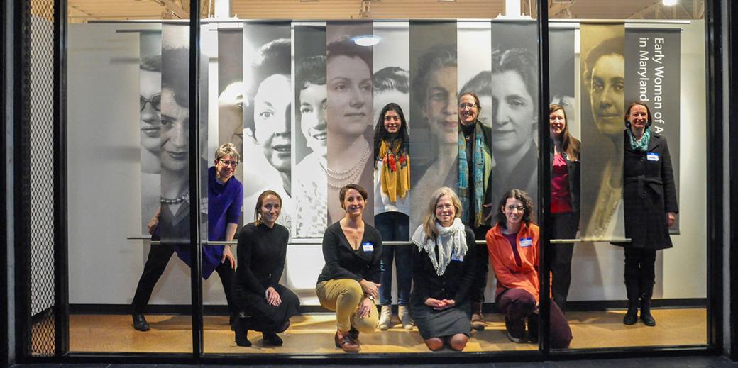 Women posing in front of hanging panels of the women MD architects from 1920s to 1960s.