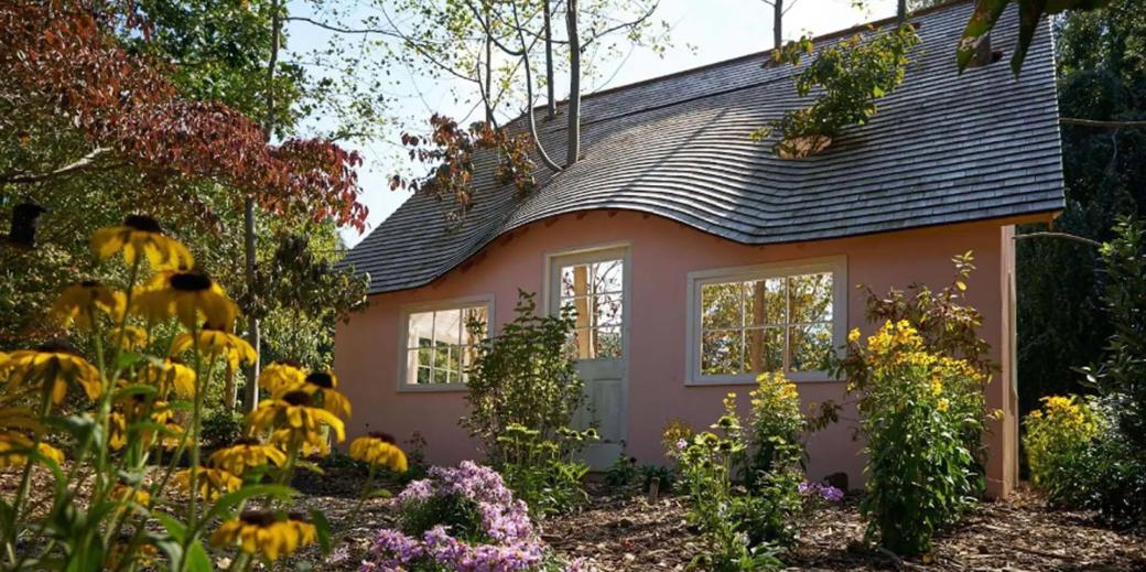 Pink cottage surrounded by flowers and trees.