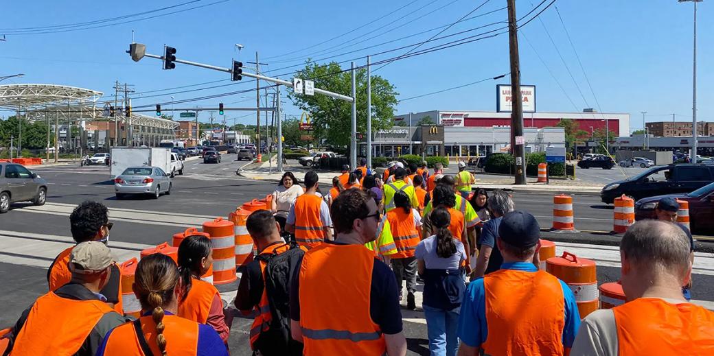 People in orange and yellow safety vests walk along the Purple Line corridor. 
