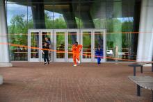The people running toward the camera. Man in the middle is wearing an orange jumpsuit and there is orange tape serving as obstacles.