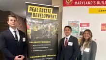People dressed in suits standing by a Real Estate Development Banner