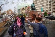 Students pointing towards buildings, Henry Longfellow statue in the background.