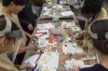 People gathering around a table, working on colorful mosaics.