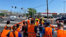People in orange and yellow safety vests walk along the Purple Line corridor. 