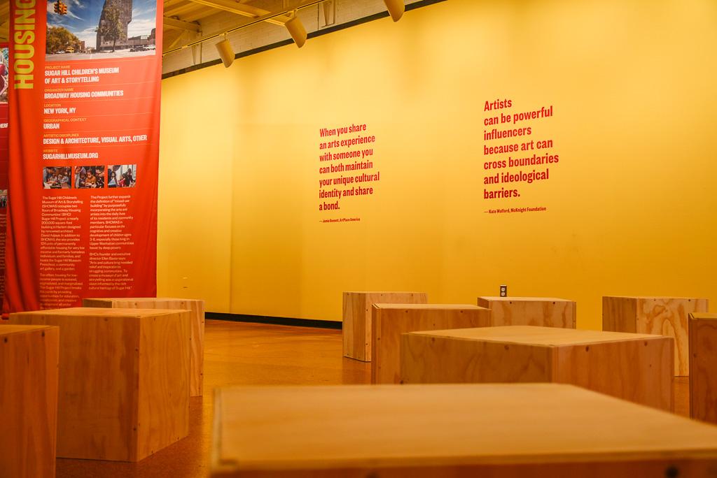 Wooden boxes on floor and quotes on yellow back wall.