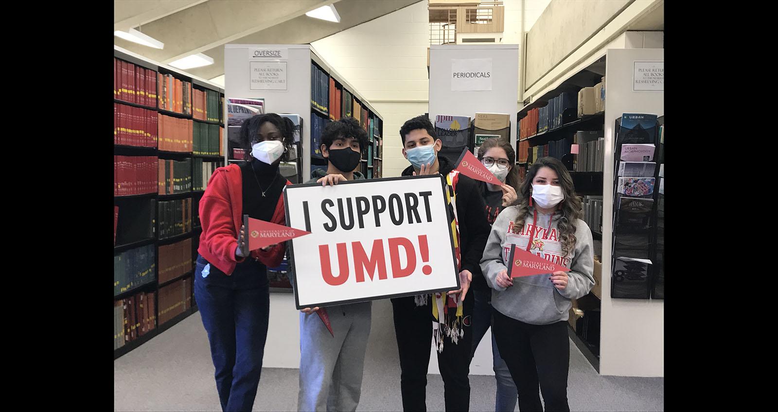 Students in the library with facemasks, holding a sign saying "I Support UMD"