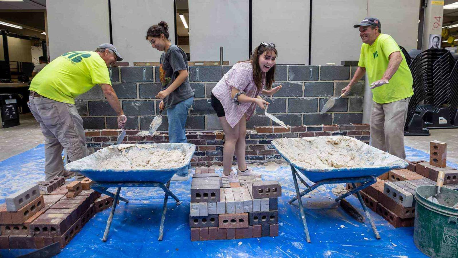 Student laughing while brick laying. Other students and Potomac Valley Brick and Supply workers. 