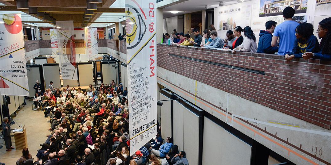 Top view of a mezzanine filled with lots of people standing and sitting, attending a lecture