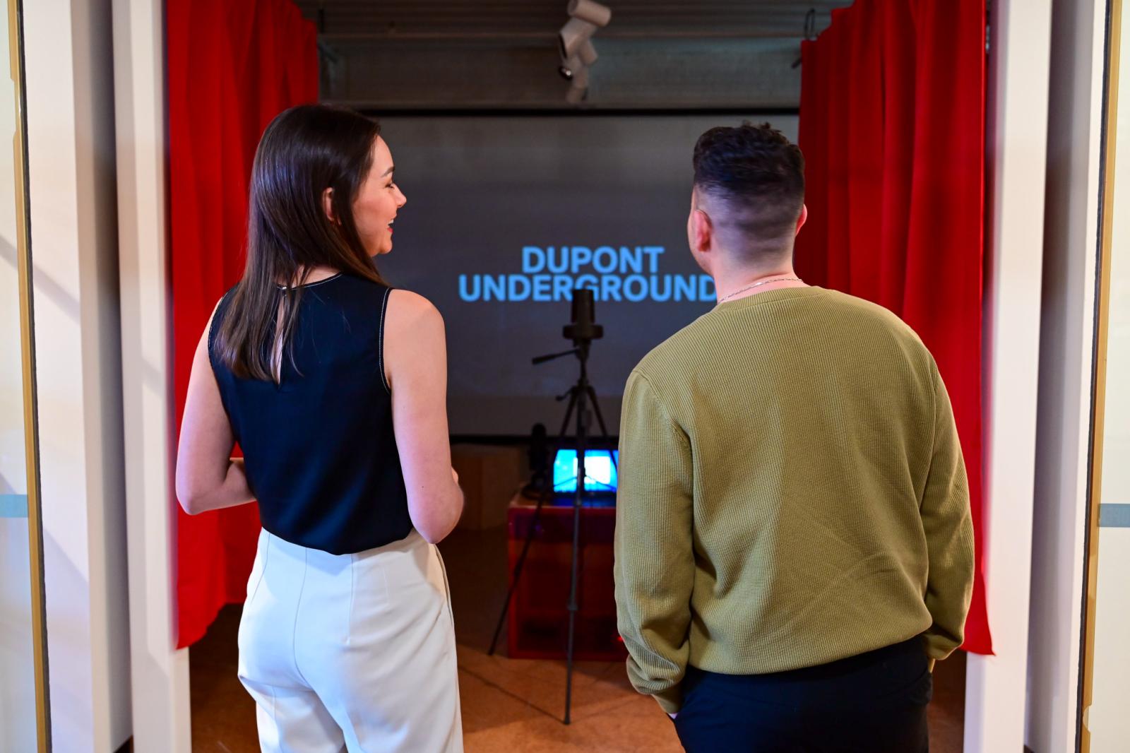 People standing in front of red curtains, a projection reads The Dupont Underground in the background