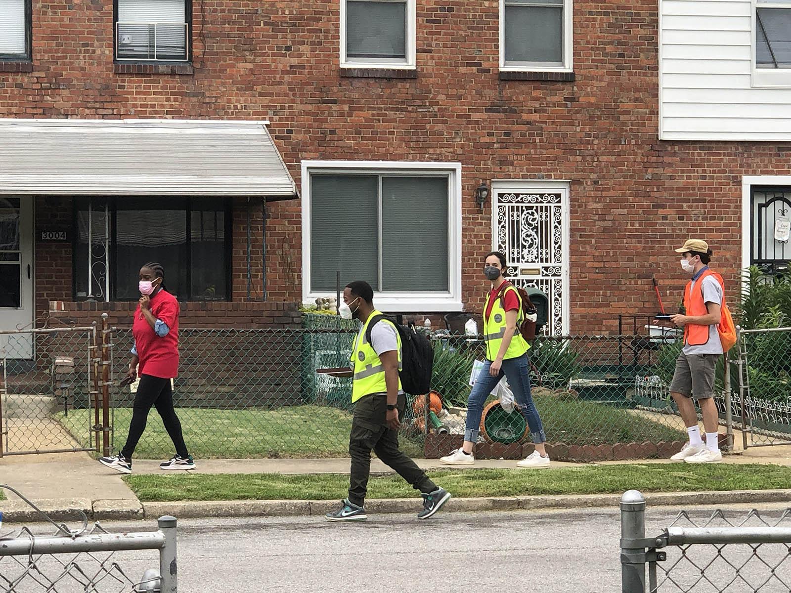 People walking in a neighborhood, wearing reflective vests and masks