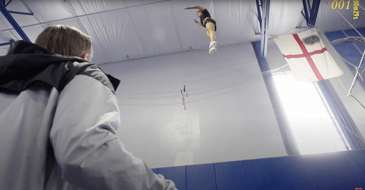 Woman jumping high on a trampoline and her coach looking up.