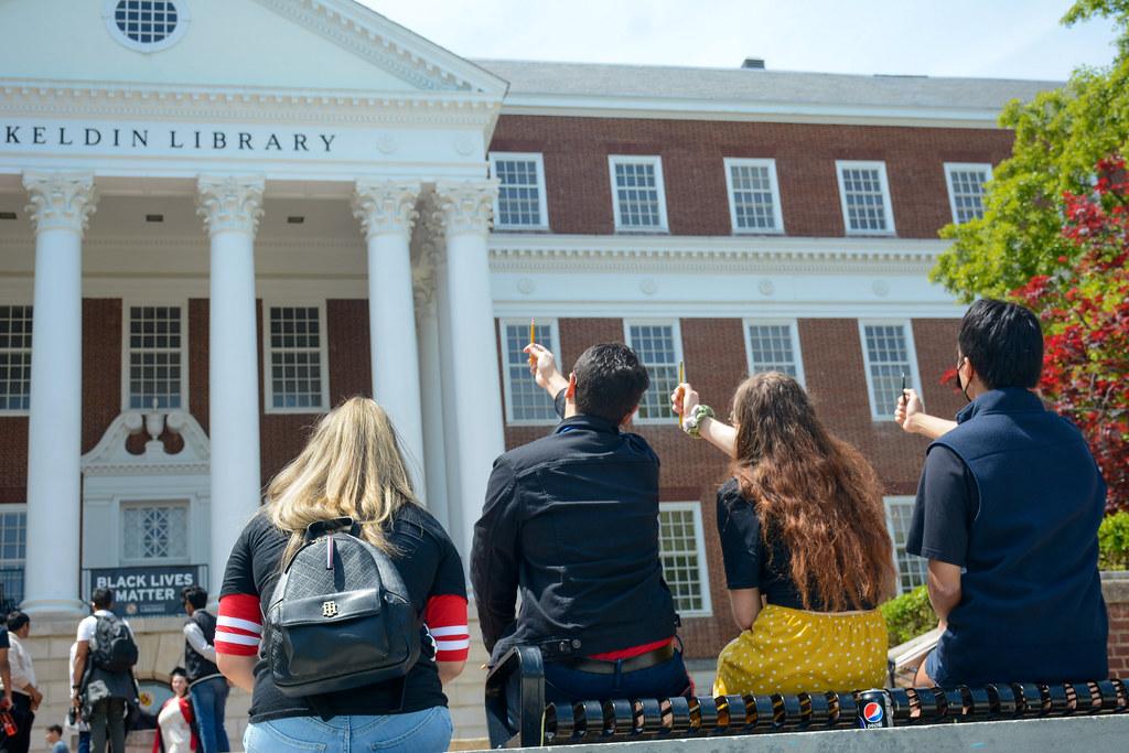 Professor Abrams and Students holding up pencils to McKeldin Library