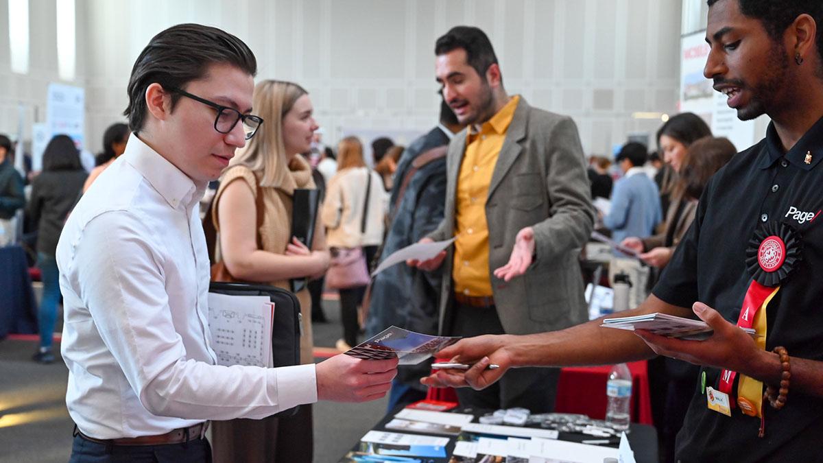 People exchanging pamphlets and others talking in the background during a career fair.