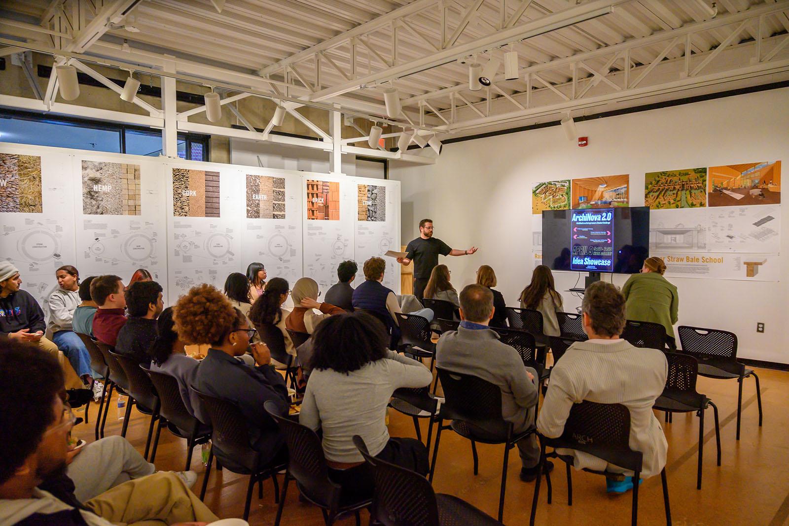 Instructor at the front of a creative room with a digital sign that says ArchiNova 2.0
