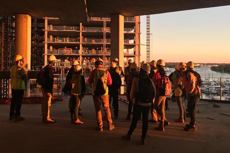 Students at a construction site wearing hard hats at sunset