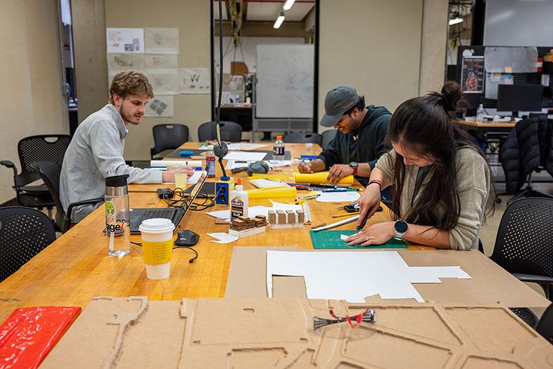 Three students working at a table and cutting materials