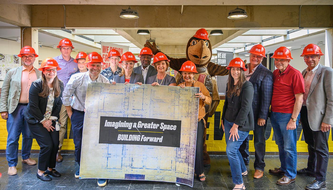 Board of Visitors and Testudo wearing hard hats standing in the mezzanine with a large blueprint that states "Imagining a Greater Space"