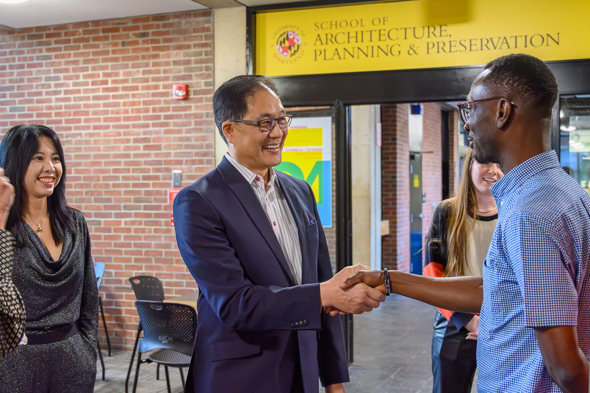 Two men shaking hands and a yellow banner behind them reads School of Architecture, Planning & Preservation