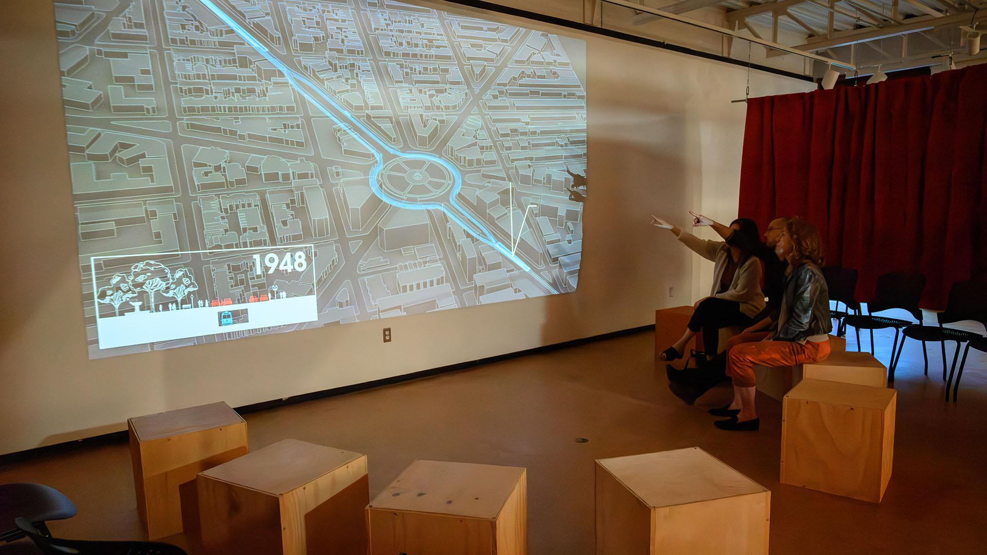 People sitting on wooden cubes and pointing to a screen of the Dupont Underground sitemap