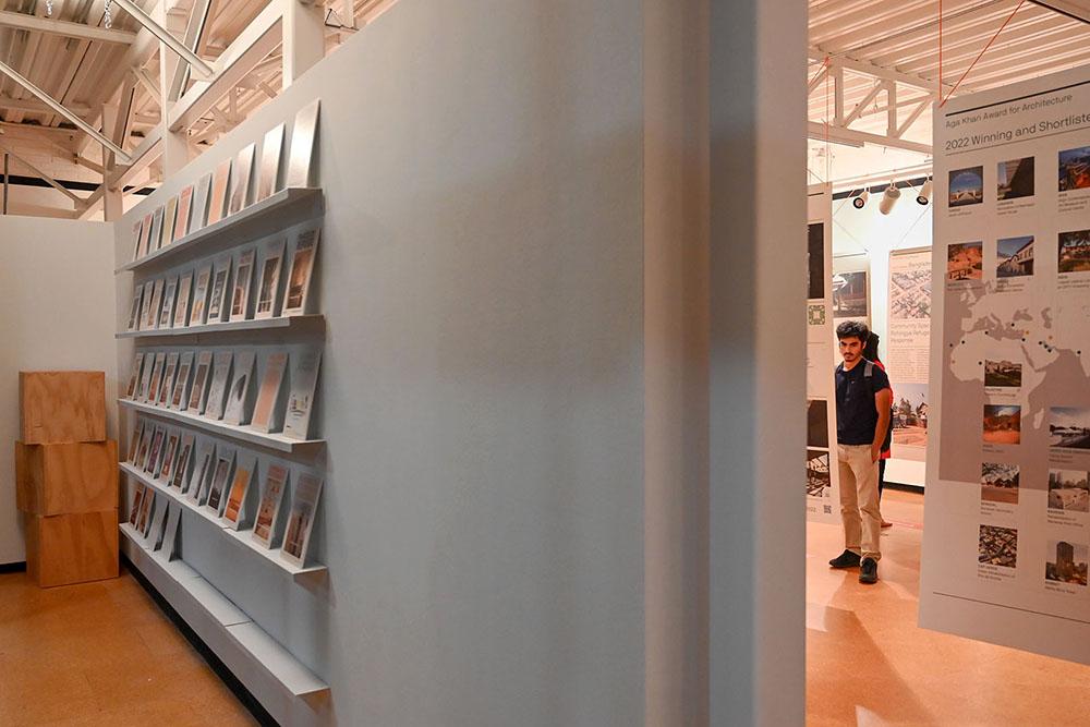 Book shelves in the foreground and a man looking at a gallery exhibit in the background with banners hanging