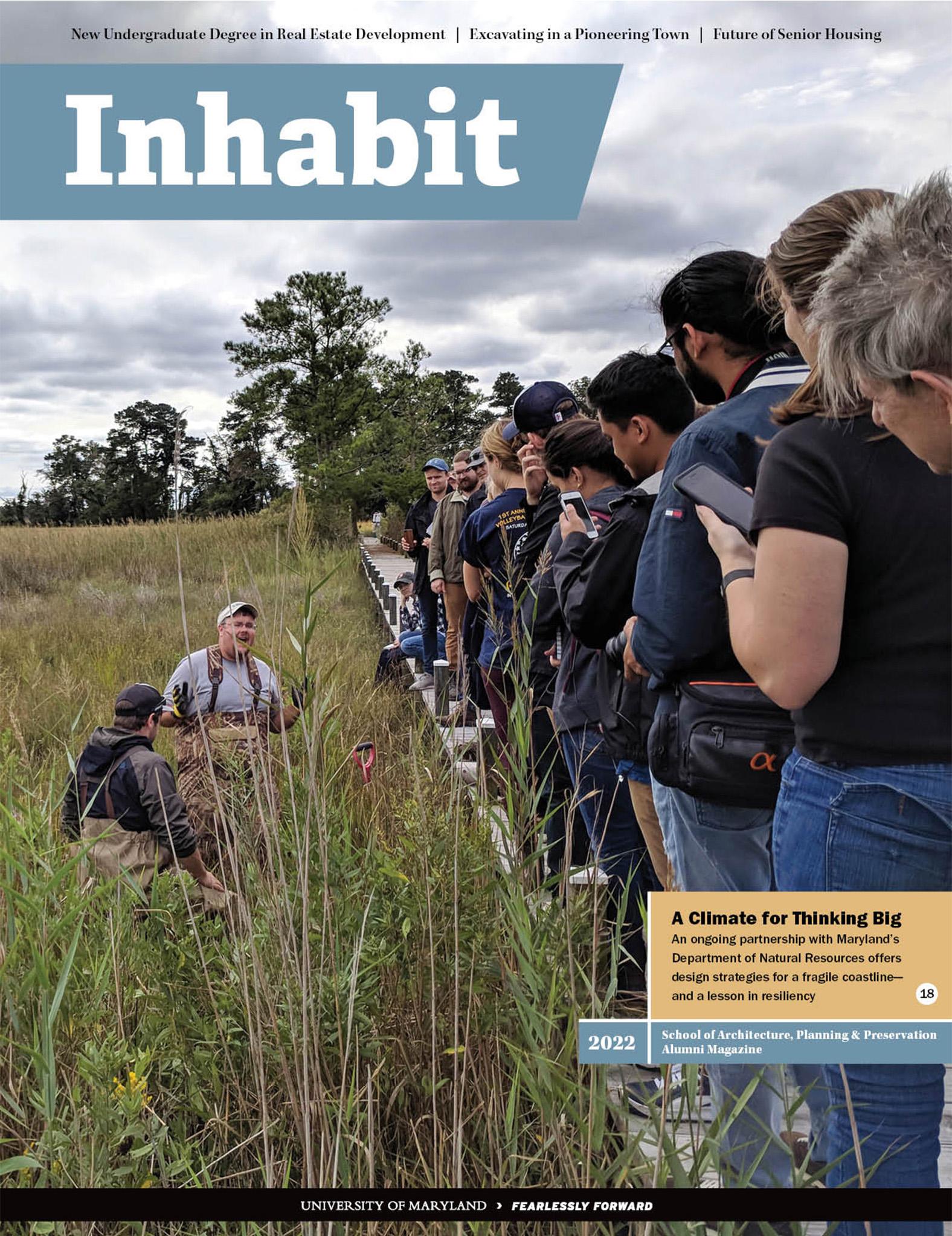 Inhabit Magazine cover of people lined up on a small bridge looking down at a man speaking in tall grass