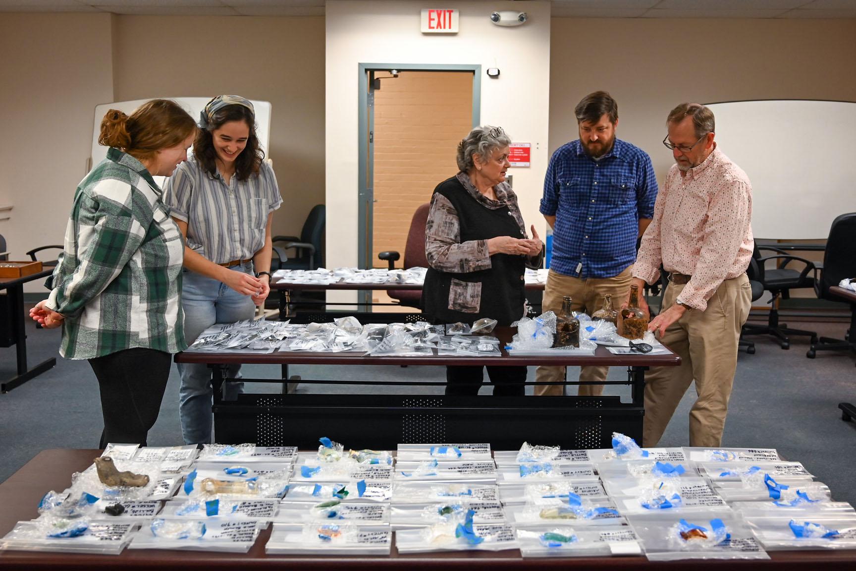 Students and professors looking at artifacts, beyond many that are labeled and inventoried. 