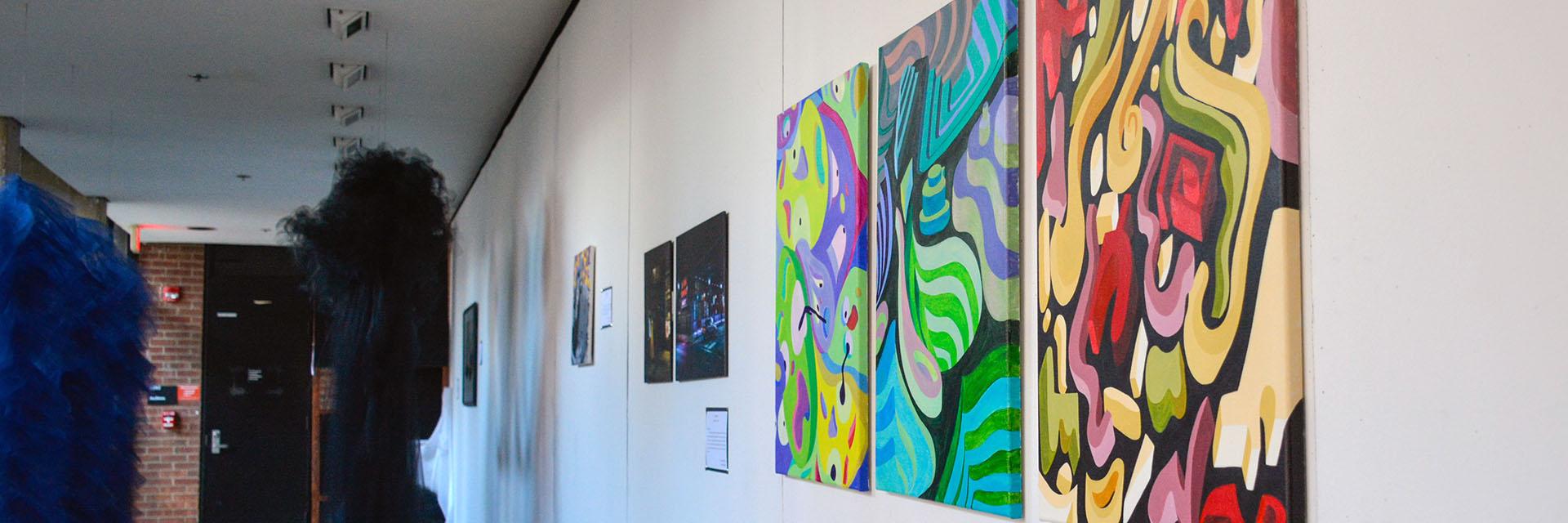 Colorful paintings in the foreground and black and blue abstract fabric hanging in the background